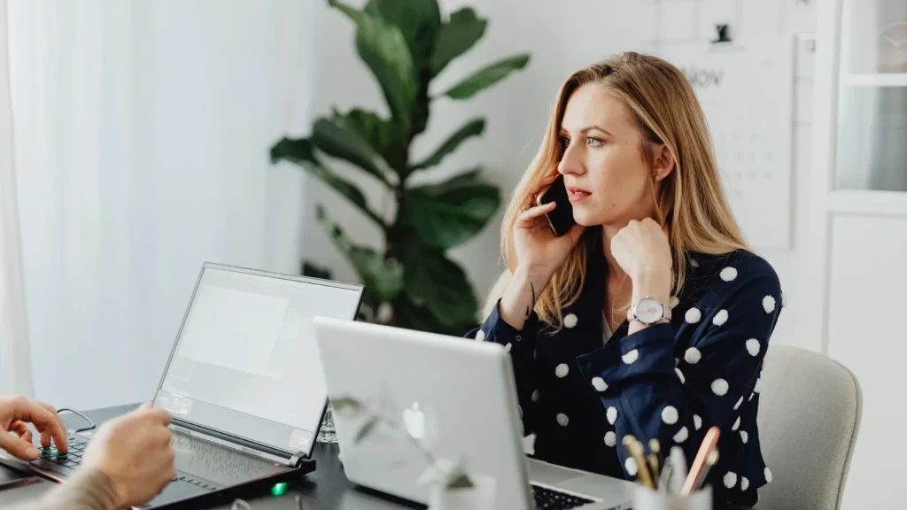 Businesswoman on a phone call while working at a laptop in a small office